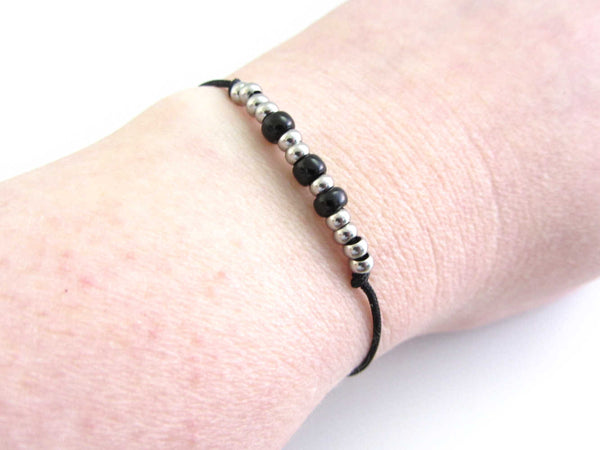 'sarah' name adjustable cord bracelet written in morse code stainless steel beads and black glass seed beads on black cord worn on wrist for others to read