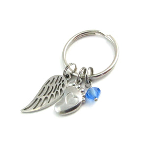 a single angel wing charm, a single foot charm with indented heart and a blue crystal charm on a keyring