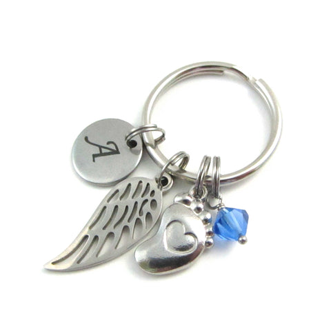 laser engraved capital initial letter disc charm, a single angel wing charm, a single foot charm with indented heart and a blue crystal charm on a keyring