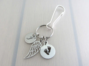 stainless steel laser engraved capital initial letter disc charm, a single angel wing and a laser engraved baby footprints charm on a bag charm with snap clip hook