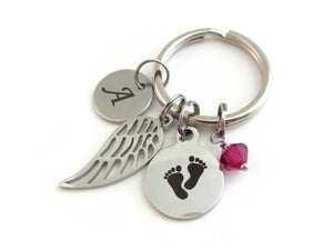 laser engraved capital initial letter disc charm, a single angel wing charm, a laser engraved baby footprints charm and a red crystal charm on a keyring