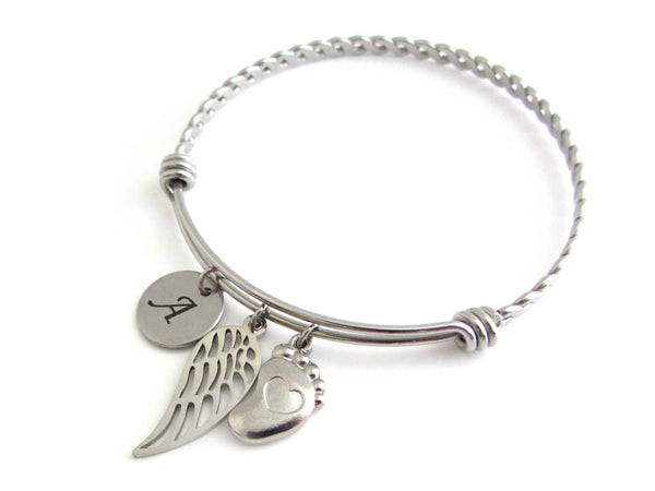stainless steel laser engraved capital initial letter disc charm, a single angel wing charm and a single foot charm with indented heart on a bangle with braided twist pattern