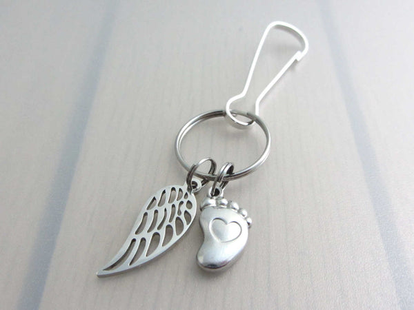 stainless steel single angel wing charm and a single foot charm with indented heart on a bag charm with snap clip hook
