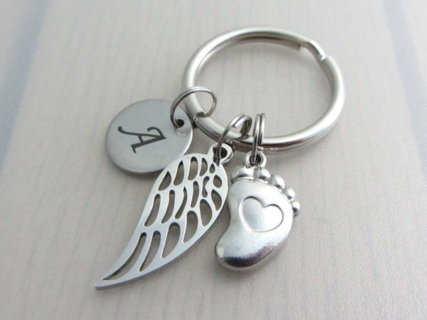 stainless steel laser engraved capital initial letter disc charm, a single angel wing and a single foot charm with indented heart on a keyring