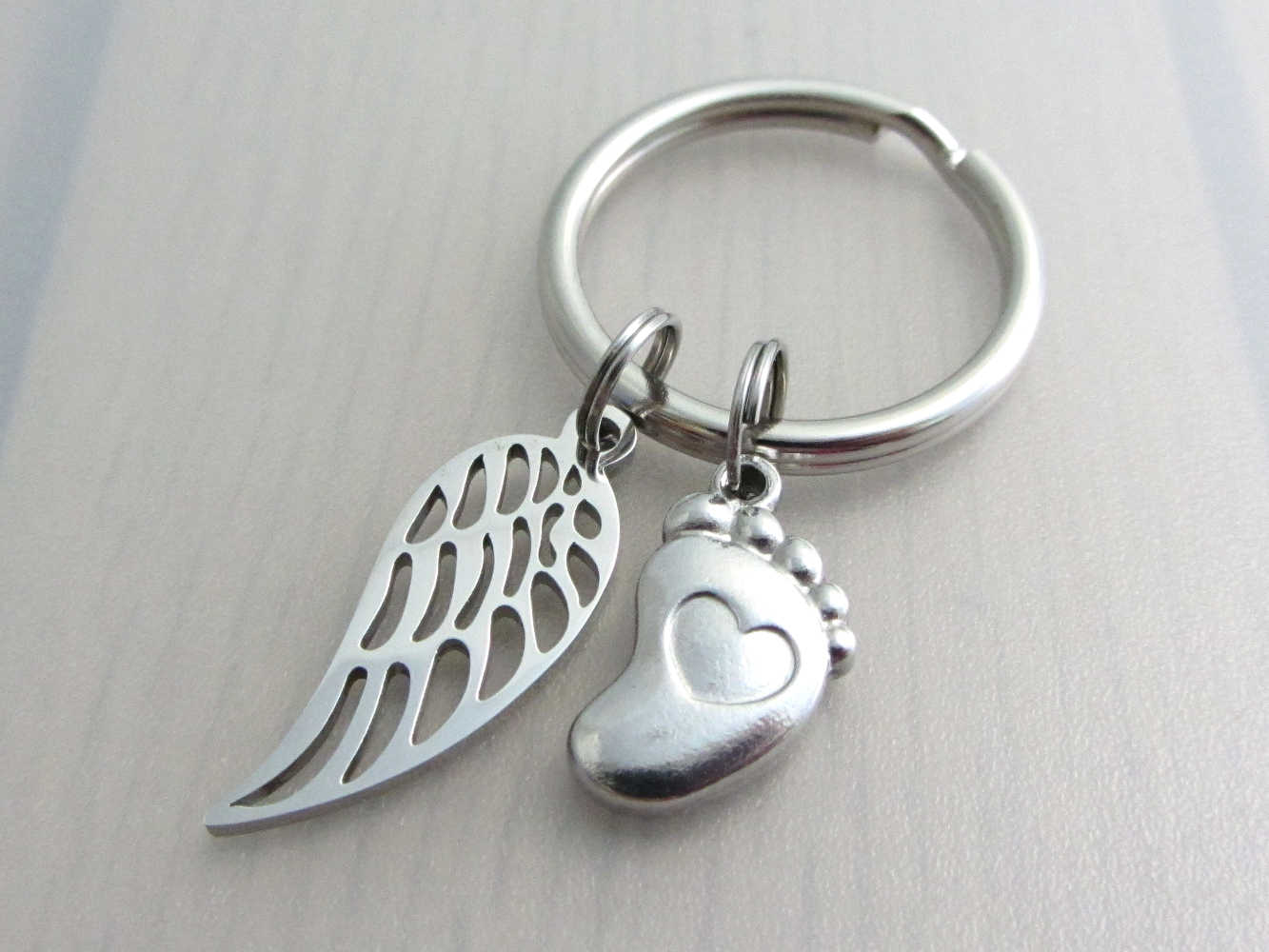 stainless steel single angel wing charm and a single foot charm with indented heart on a keyring