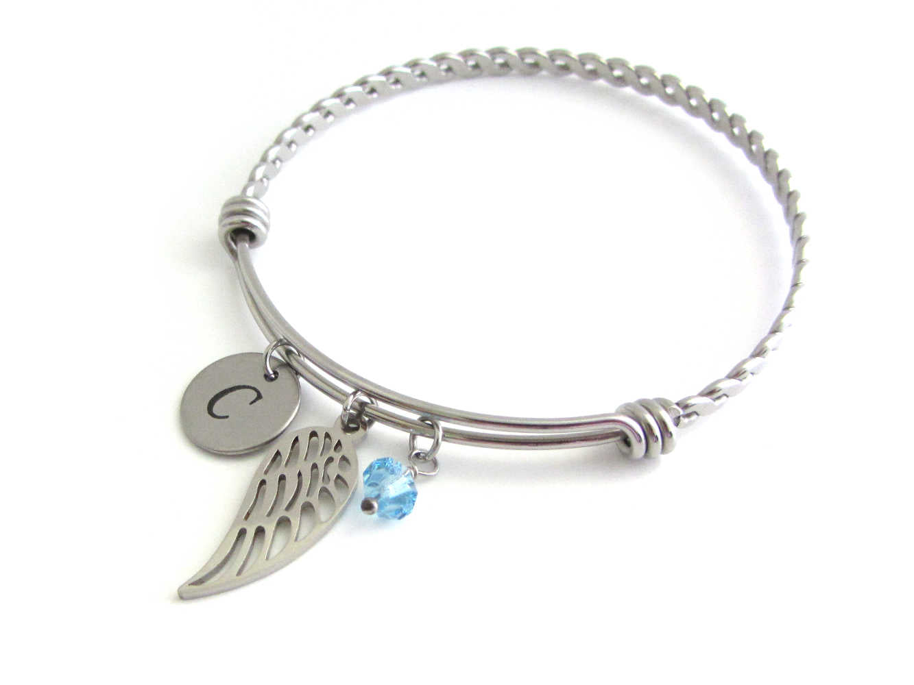 stainless steel laser engraved capital initial letter disc charm, single angel wing charm and a light blue crystal charm on a bangle with braided twist pattern