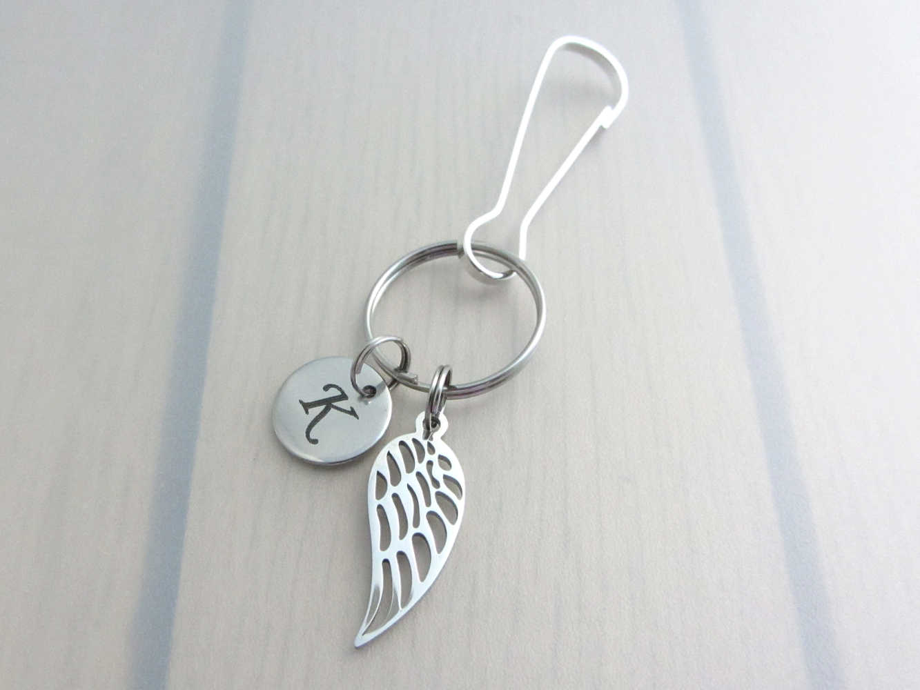 stainless steel laser engraved capital initial letter disc charm and single angel wing charm on a bag charm with snap clip hook