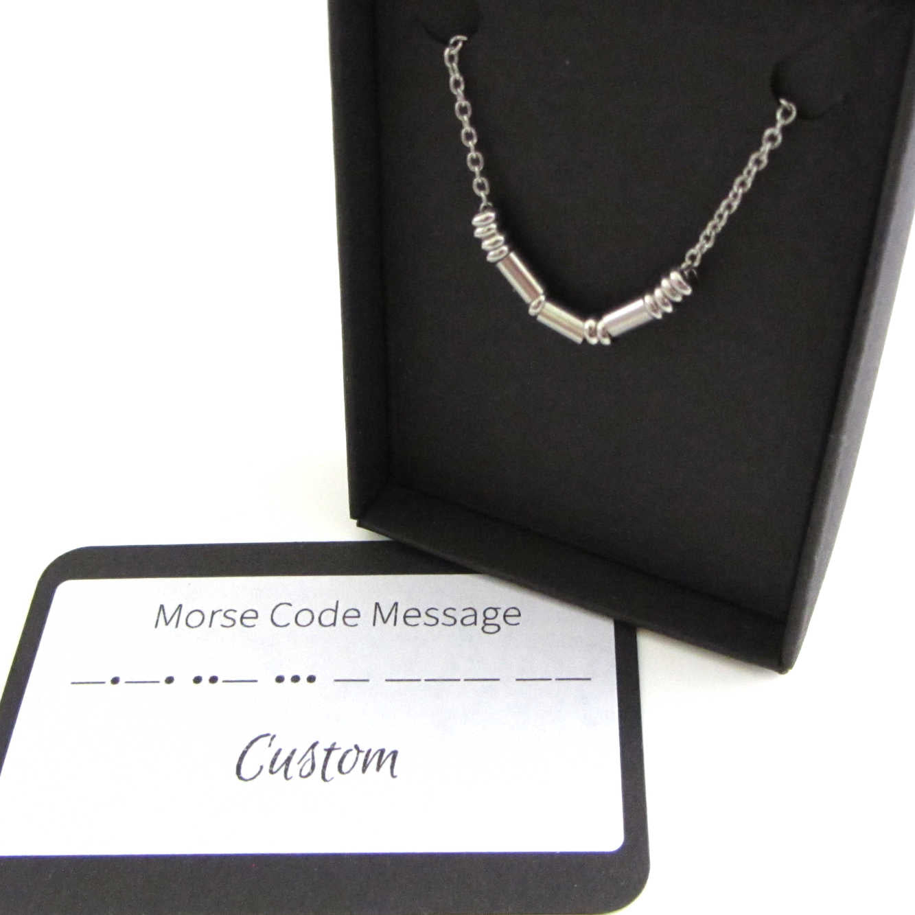 close up of 'sarah' name necklace written in morse code stainless steel beads on a stainless steel chain shown in box with custom morse code message card