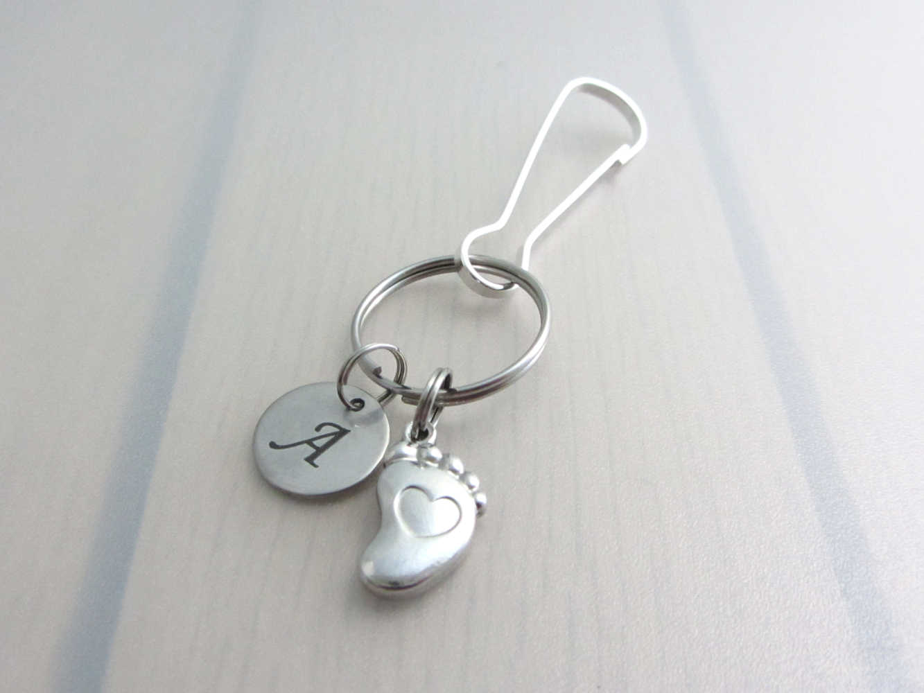 stainless steel laser engraved capital initial letter disc charm and a single foot charm with indented heart on a bag charm with snap clip hook