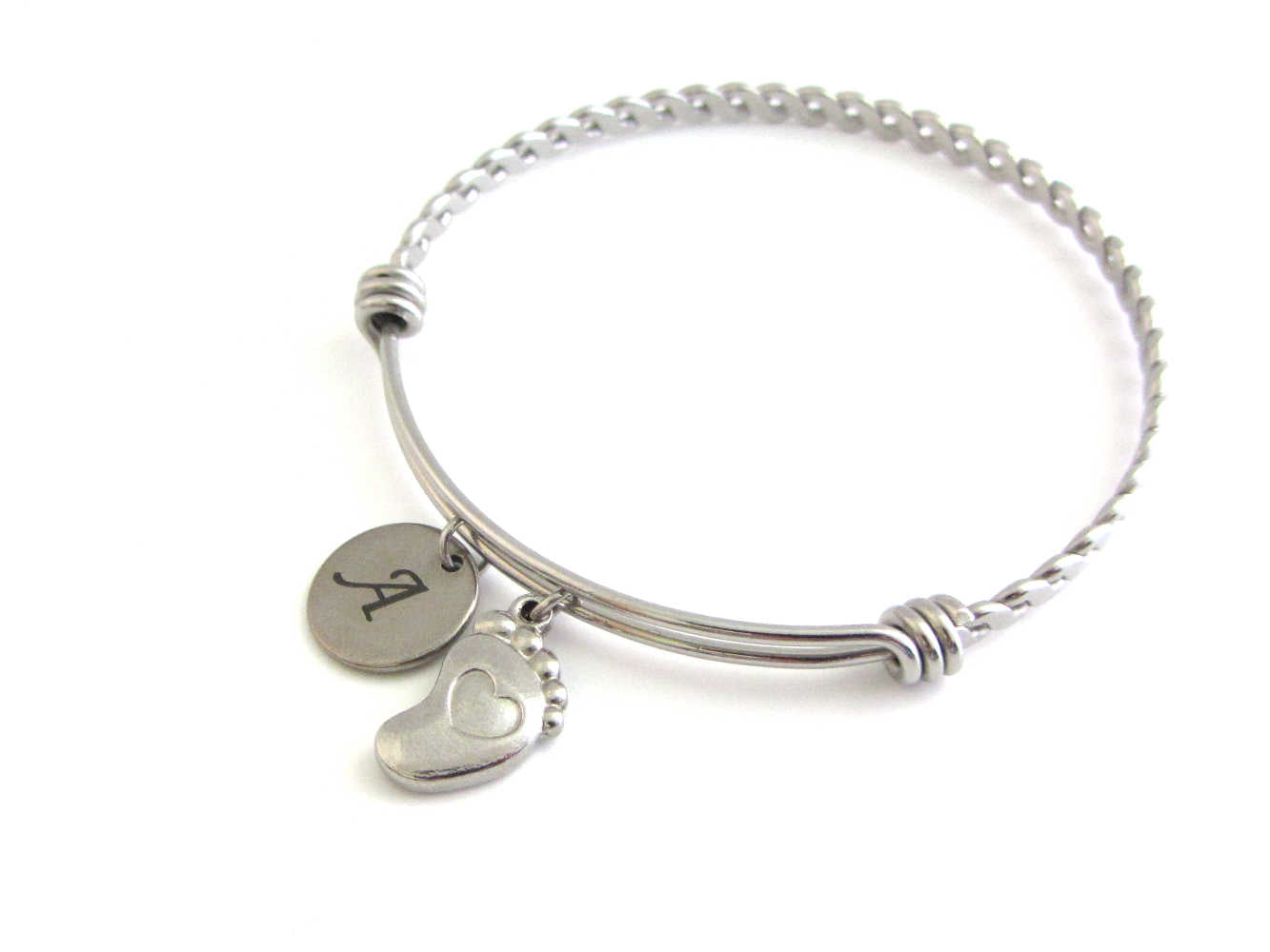stainless steel laser engraved capital initial letter disc charm and a single foot charm with indented heart on a bangle with braided twist pattern
