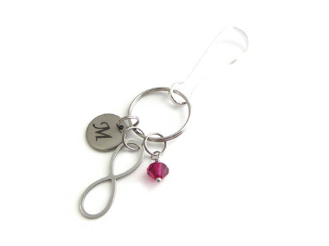 stainless steel laser engraved capital initial letter disc charm, an infinity charm and a red crystal charm on a bag charm with snap clip hook