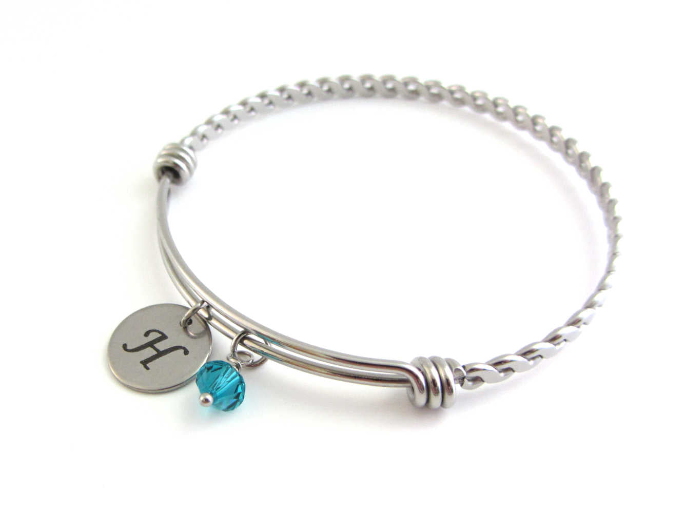 laser engraved capital initial letter disc charm and a blue green crystal charm on a bangle with braided twist pattern