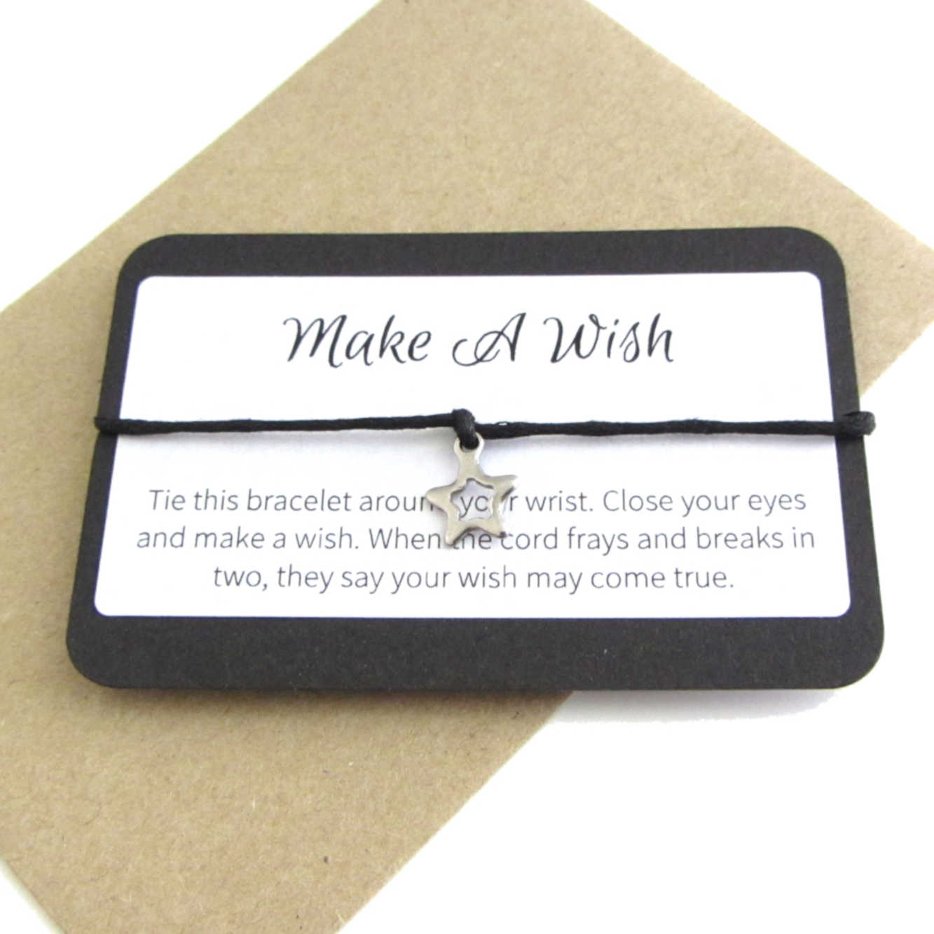 stainless steel hollow star charm on black cord string attached to a message card stating 'make a wish' and note to make a wish when tying the bracelet around a wrist with a brown craft paper envelope