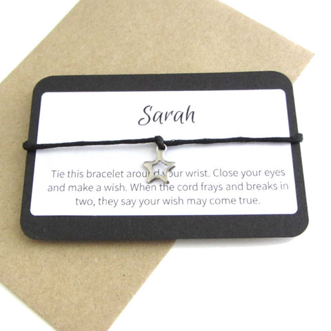 stainless steel hollow star charm on black cord string attached to a message card stating 'sarah' and note to make a wish when tying the bracelet around a wrist with a brown craft paper envelope