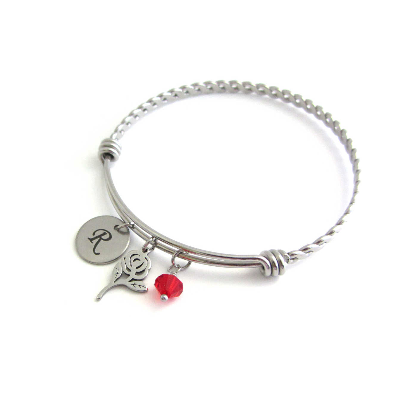 laser engraved capital initial letter disc charm, rose flower charm and a red crystal charm on a bangle with braided twist pattern