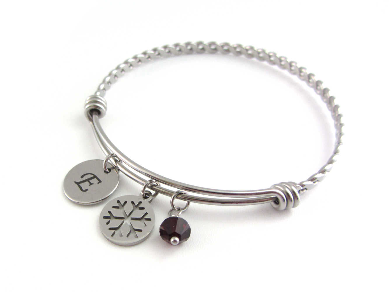 laser engraved capital initial letter disc charm, snowflake charm and a red crystal charm on a bangle with braided twist pattern