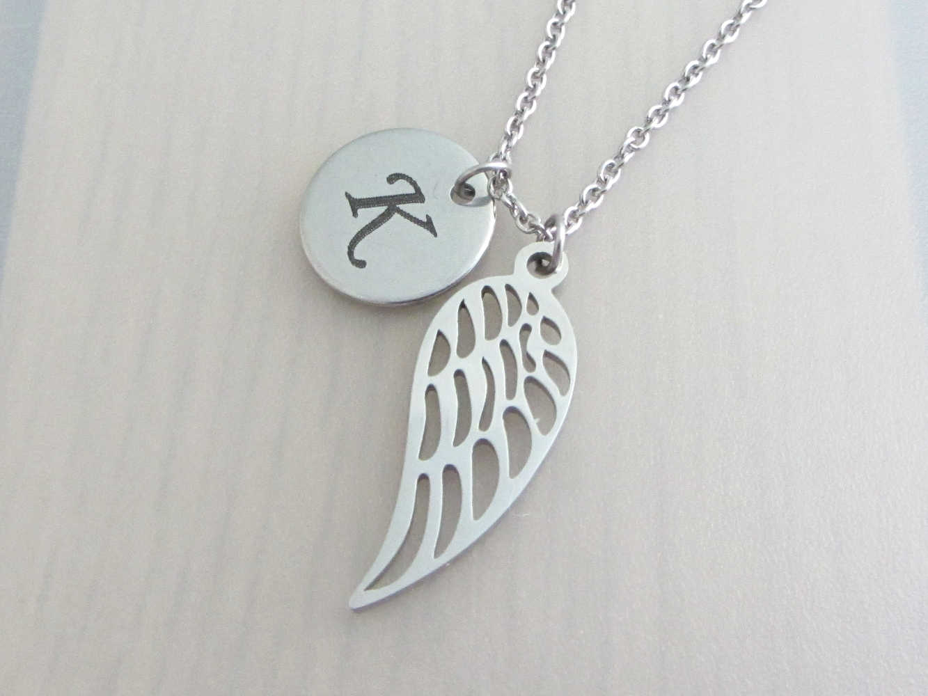 laser engraved capital initial letter disc charm and single angel wing charm on a stainless steel chain