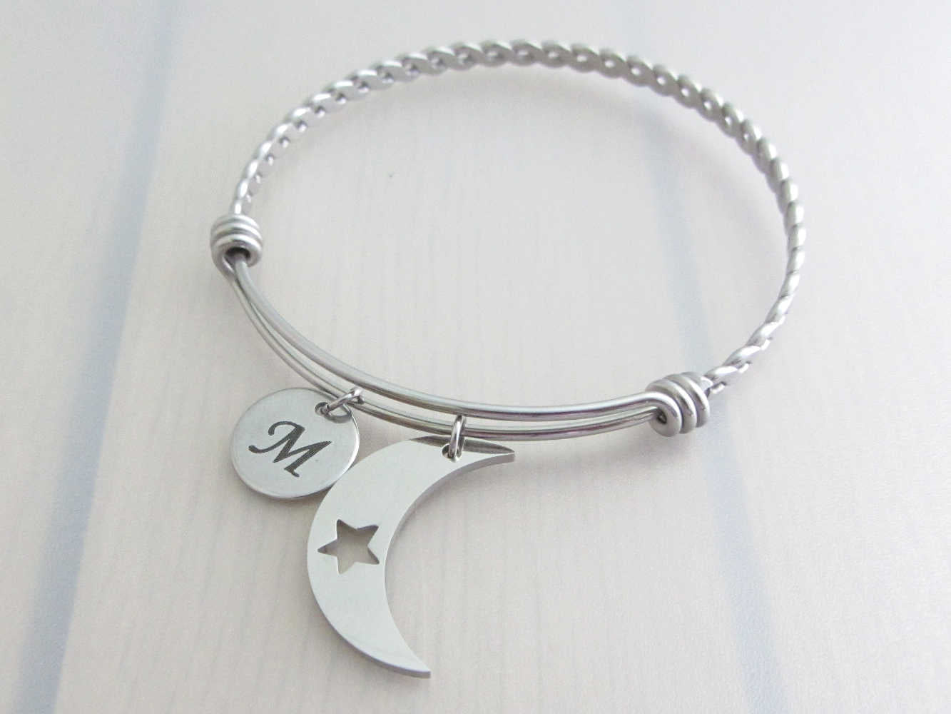 stainless steel laser engraved capital initial letter disc charm and crescent moon with cut out star charm on a bangle with braided twist pattern