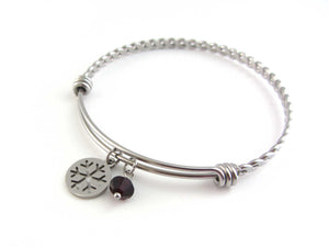 stainless steel snowflake charm and a red crystal charm on a bangle with braided twist pattern