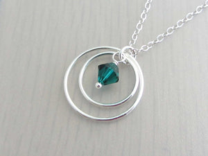 two silver circle rings and green coloured crystal charm on a silver chain