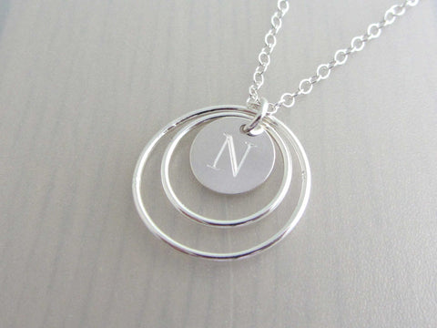 two silver circle rings and engraved capital initial letter disc charm on a silver chain