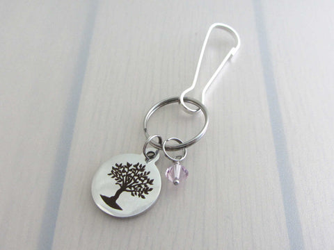laser engraved tree charm and a pale purple crystal charm on a bag charm