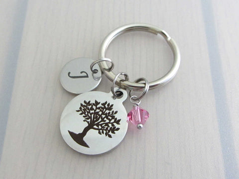 laser engraved capital initial letter disc charm, laser engraved tree charm and a pink crystal charm on a keyring
