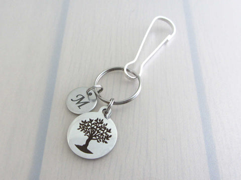 laser engraved capital initial letter disc charm and a laser engraved tree charm on a bag charm