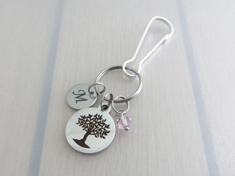 laser engraved capital initial letter disc charm, laser engraved tree charm and a pale purple crystal charm on a bag charm
