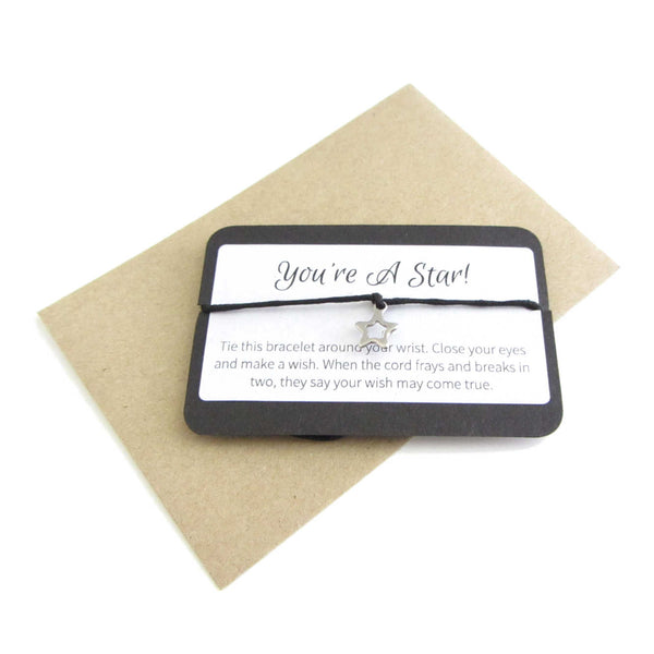 stainless steel hollow star charm on black cord string attached to a message card stating 'you're a star' and note to make a wish when tying the bracelet around a wrist with a brown craft paper envelope