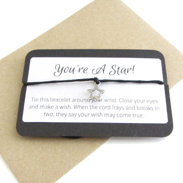 stainless steel hollow star charm on black cord string attached to a message card stating 'you're a star' and note to make a wish when tying the bracelet around a wrist with a brown craft paper envelope